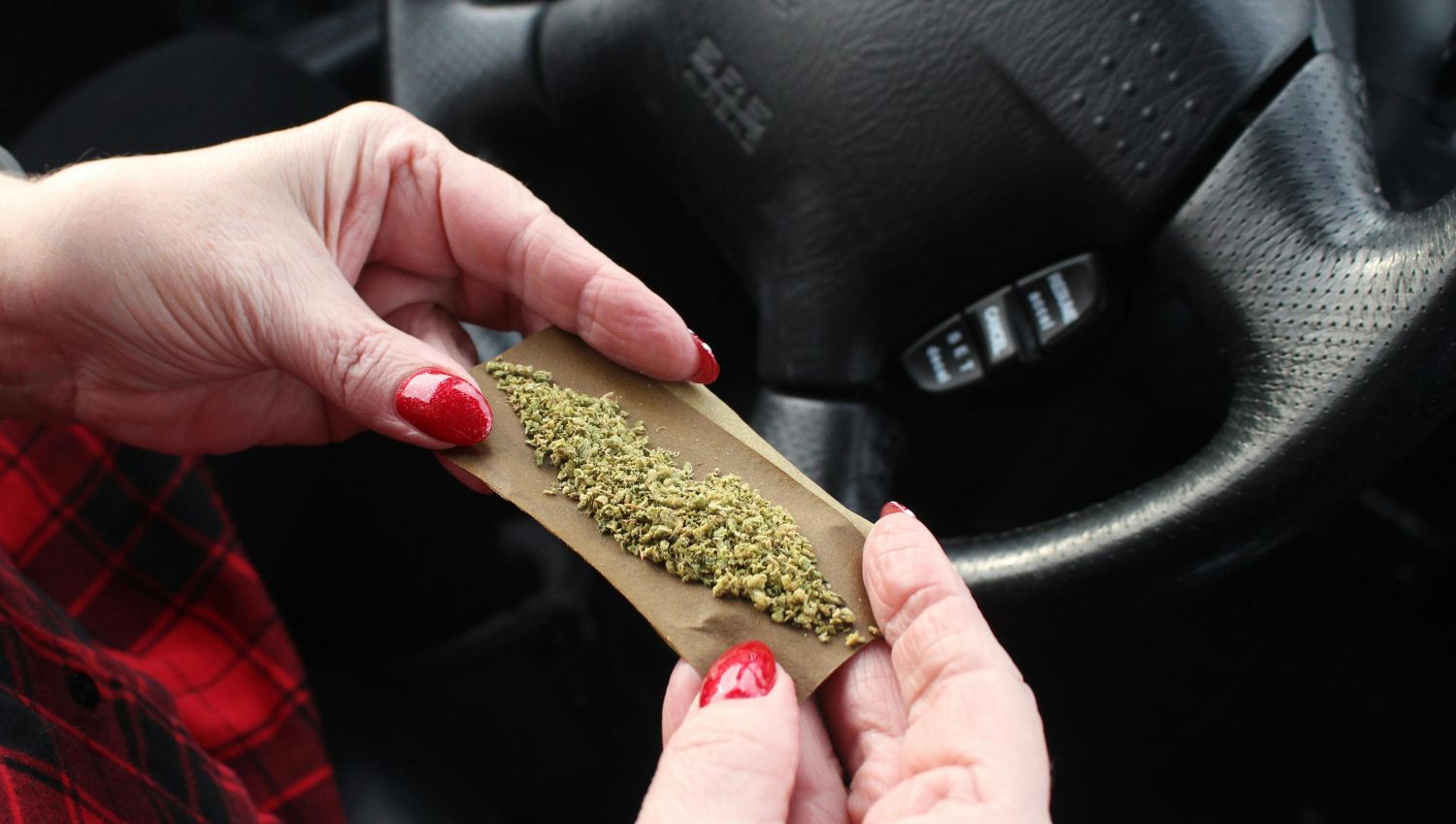 A woman rolls a marijuana joint in a car